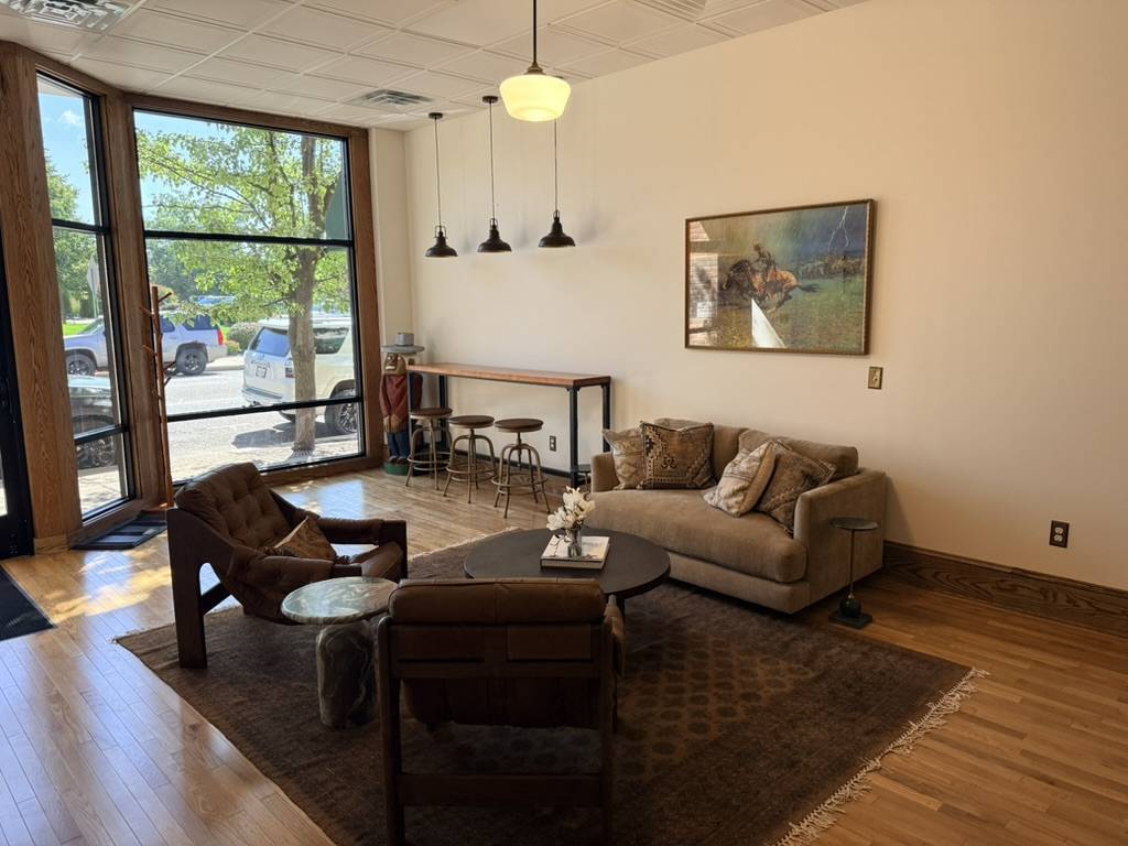 Sofas and lounge chairs at Homestead’s large front window, with café tables and the long meeting room behind.