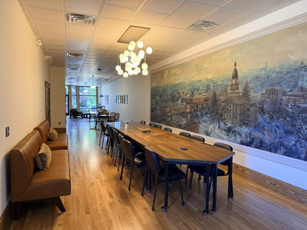Homestead’s long meeting table beside the painted panorama of Hillsdale, with oak floors and the lounge beyond.