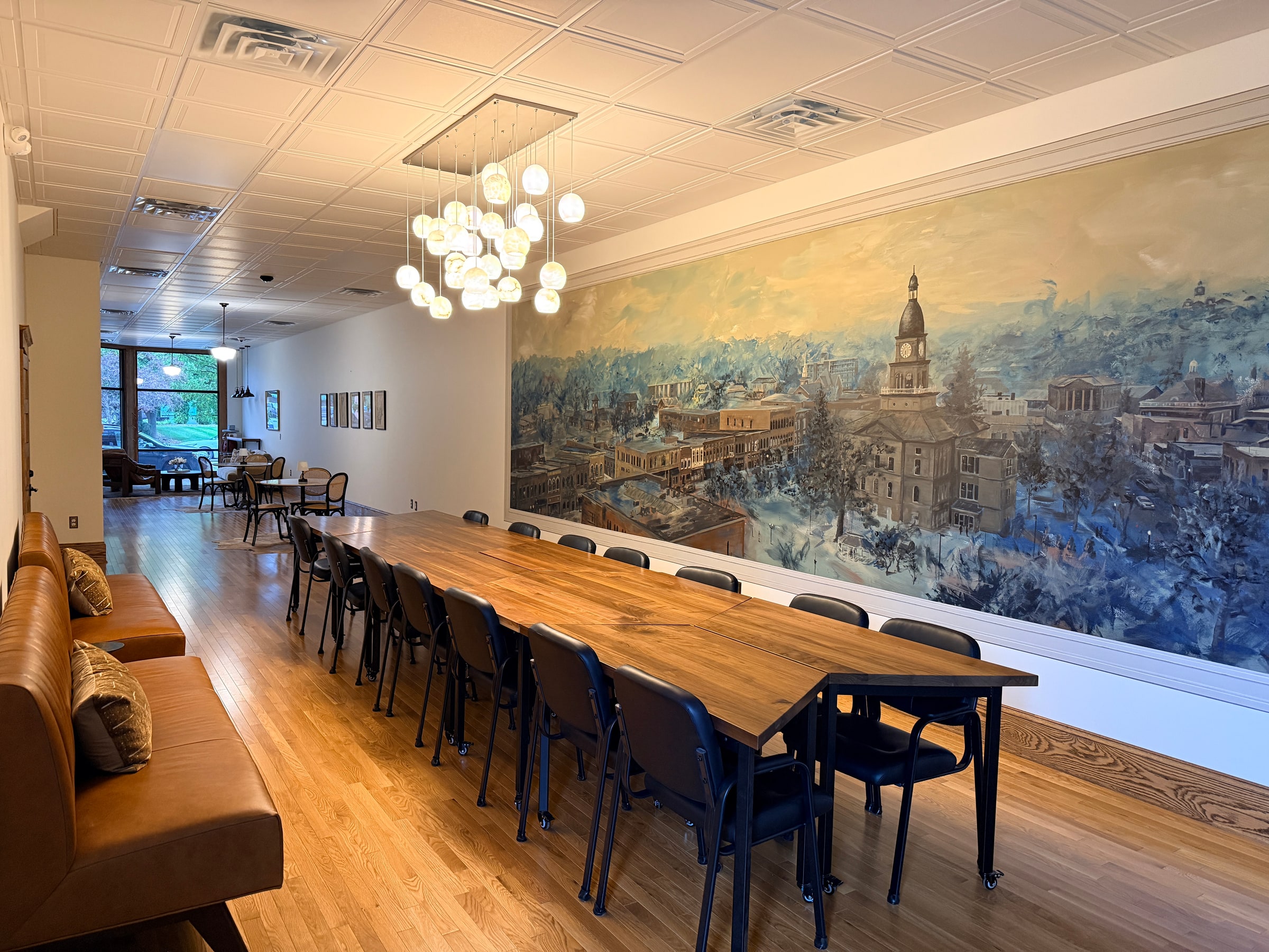 The long table beneath a chandelier and pressed tin ceiling, beside the Hillsdale mural.